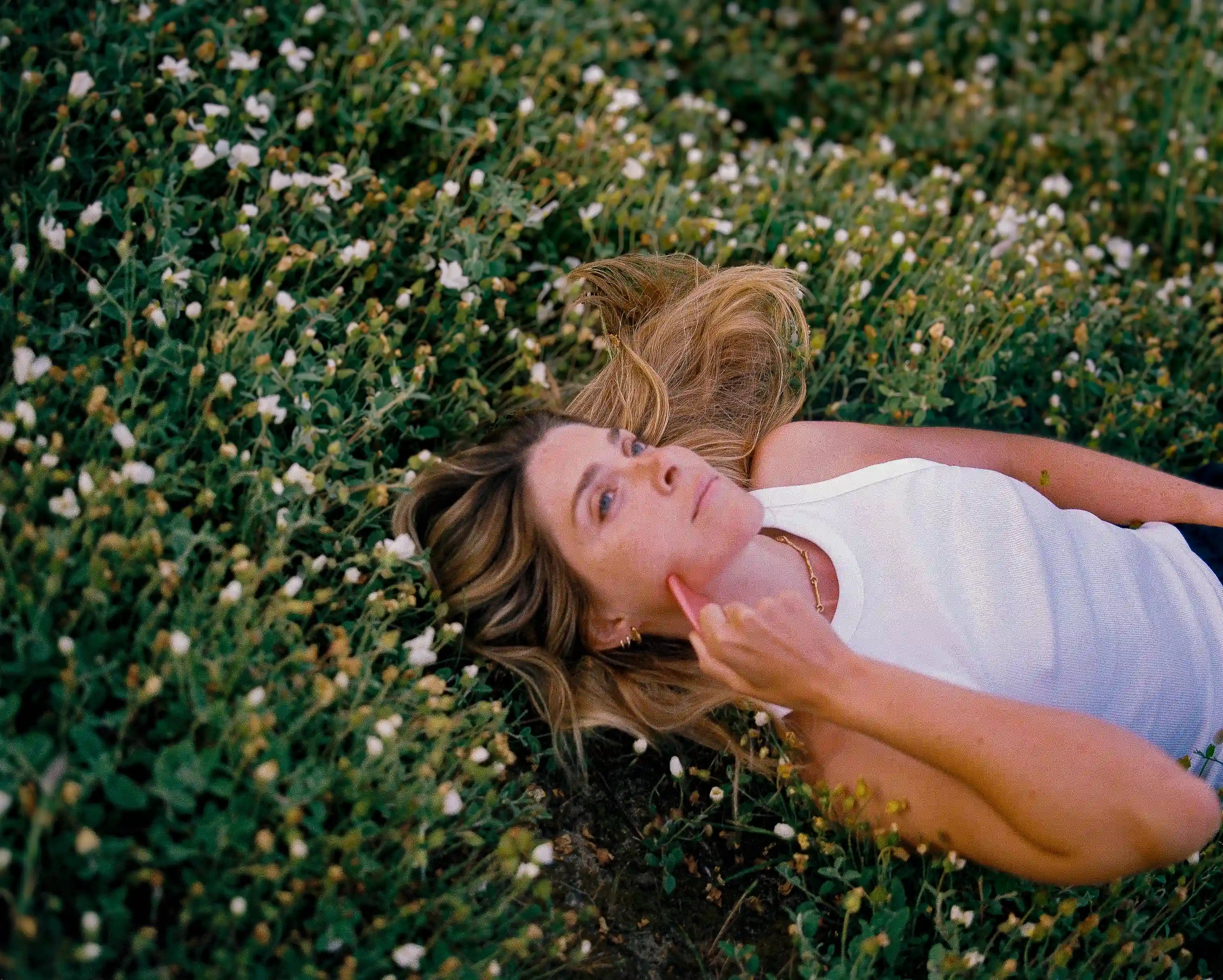 Une femme est allongée dans des fleurs et se masse le visage avec un guasha.