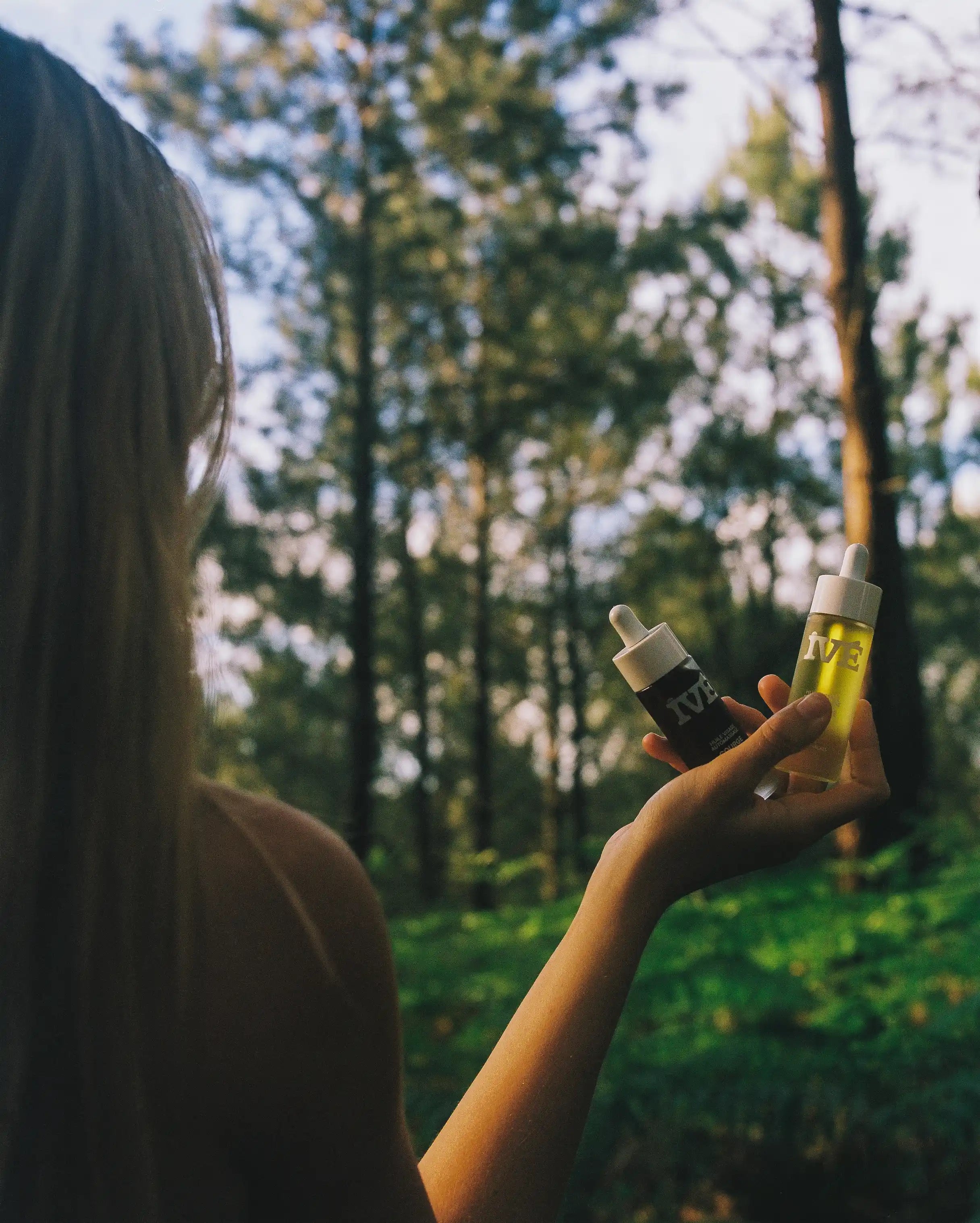 Une femme tient deux huiles dans la main dans une forêt